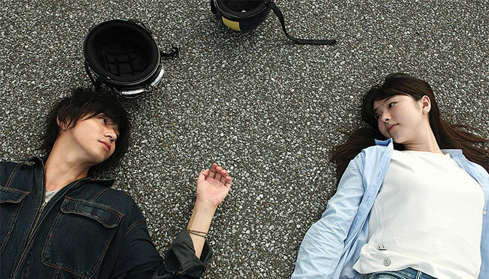 A boy and a girl lay on the asphalt staring at one another
