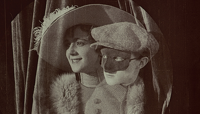A person in disguise peaks over the shoulder of a woman in a big hat