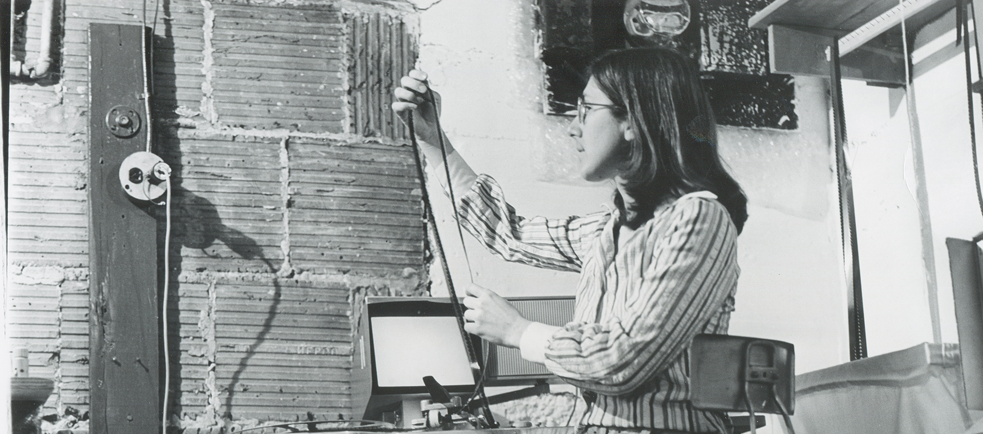 A black-and-white archive image of Julia Reichert seated and looking at a reel of film in her studio