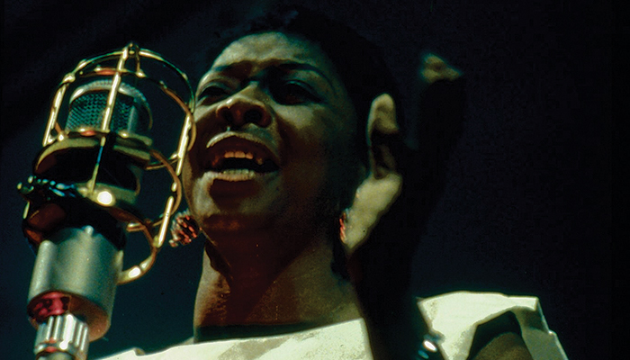 Dinah Washington, seen from neck up, sings into a large bullet microphone in a scene from the documentary Jazz on a Summer's Day