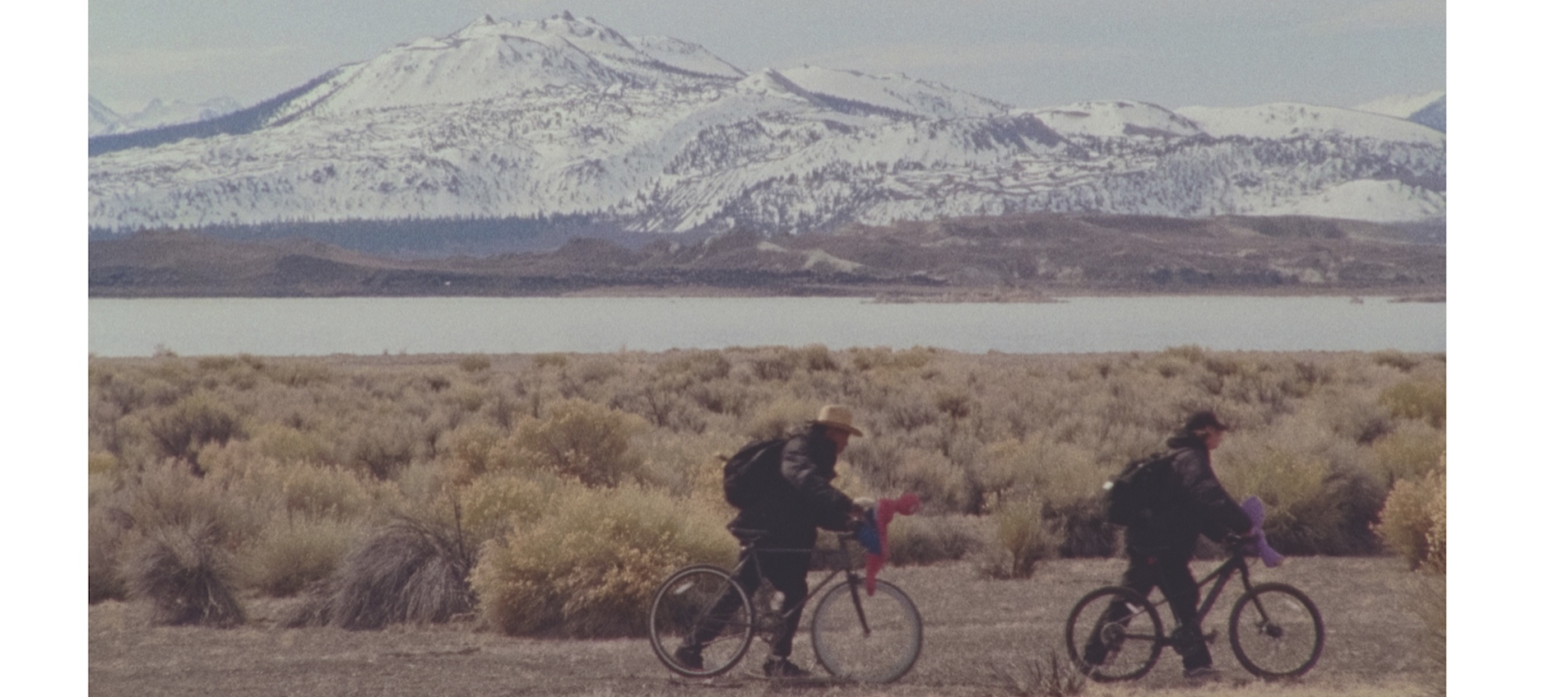 Two teenage boys ride bikes against a gray mountain-filled background in an image from artist Stanya Kahn's short film No Go Backs