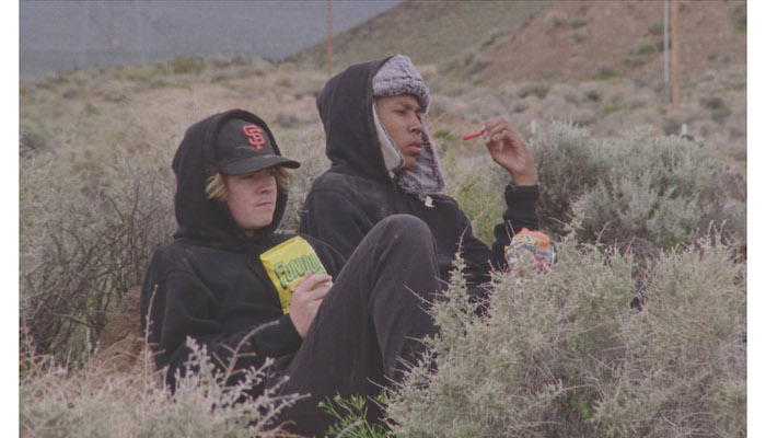 Two teenage boys in parkas sit in the brush near the Sierra Nevada mountain range in a scene from Stanya Kahn's short film No Go Backs