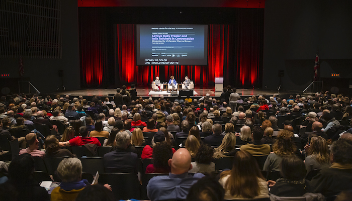 Rear view of a large audience for the 2020 Lambert Family Lecture. Julia Reichert, LaToya Ruby Frazier, and US Senator Sherrod Brown can be seen sitting center stage in the distance in front of a large projection screen