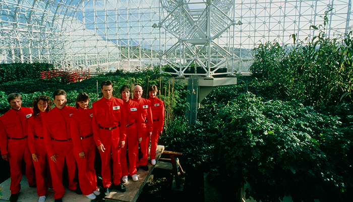 eight men and women in red uniforms in a metal and glass green house