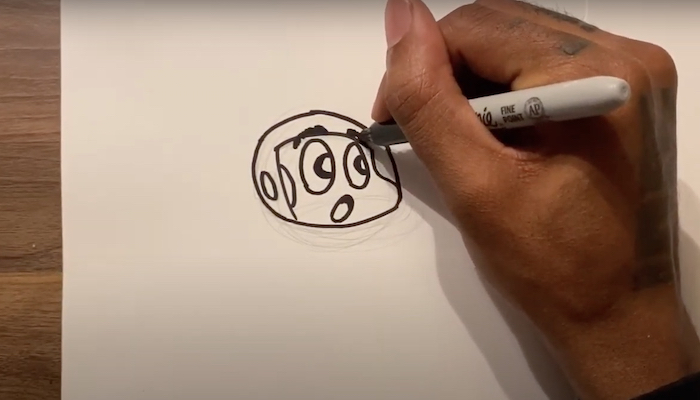 The hand of artist Hakim Callwood draws the head of his cartoon character Spaceboy