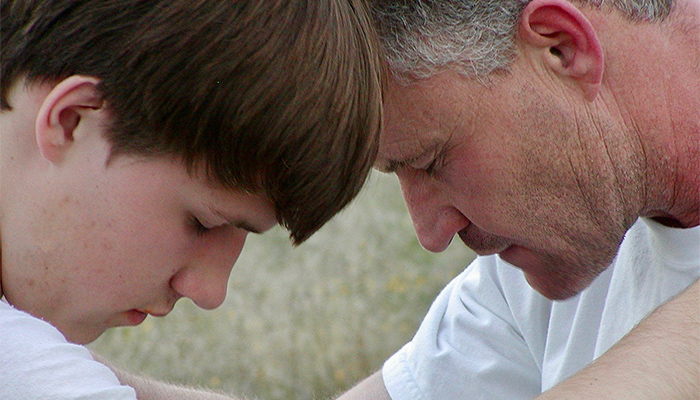 A father and child, Ryan and Rob Robertson, pray together touching foreheads.
