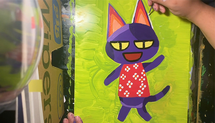 The hand of artist Bethani Blake paints a colorful portrait of Bob the Cat from the videogame Animal Crossing