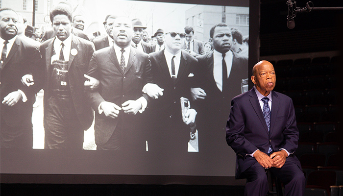 Rep. John Lewis stands in front of a projection of a historic black-and-white photo