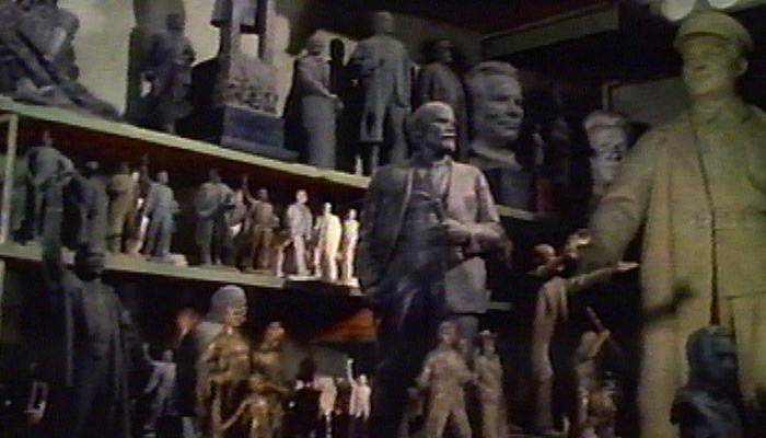 A warehouse full of old Soviet monuments, with a statue of Lenin at the center of the shot
