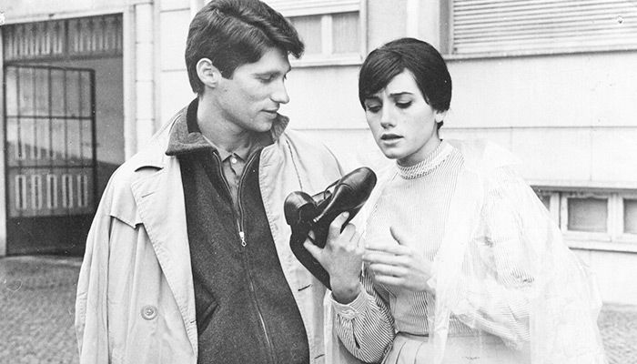 A black-and-white still of the film's young couple Julio and Ilda, with the latter examining a pair of shoes