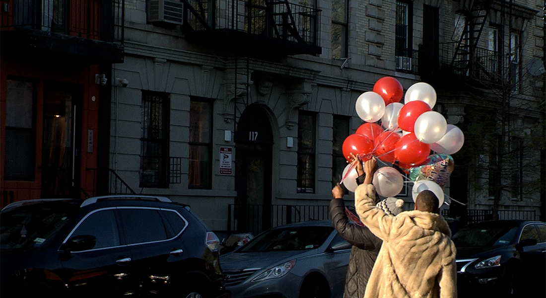 Two people walk down a city street carrying red and white balloons.