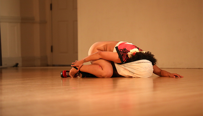 Awilda Rodríguez Lora kneels on a wood floor with a shirt over her head while removing a shoe