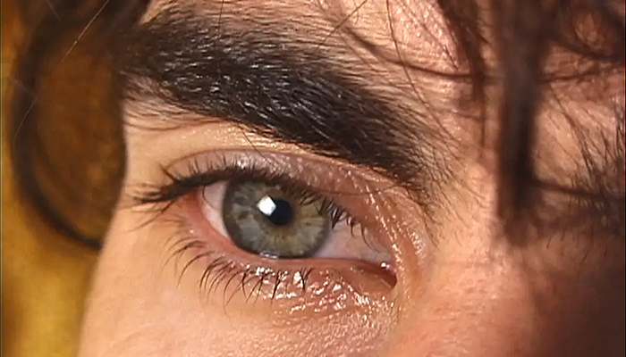 An extreme close up of a brown-haired man's right eye as he tears up