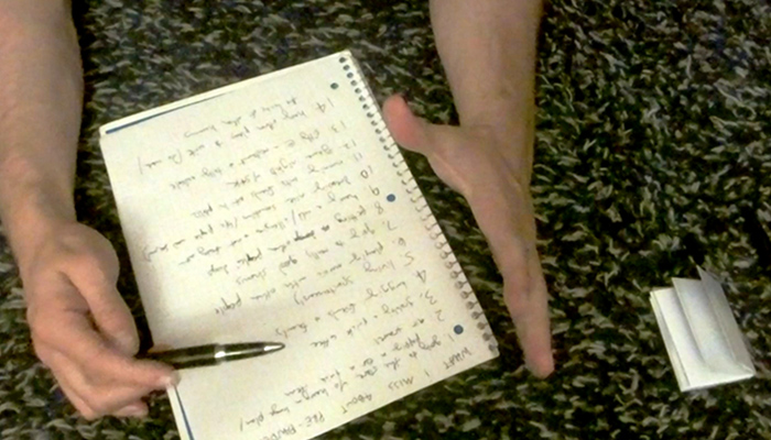 The hands of artist Noah Demland as he holds a pen and goes over a list of 'zine ideas written in a notebook