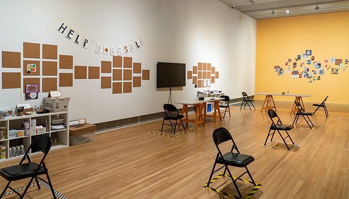 Wide shot of the gallery featuring a collection of folding chairs, artmaking materials, and images and photos on the wall
