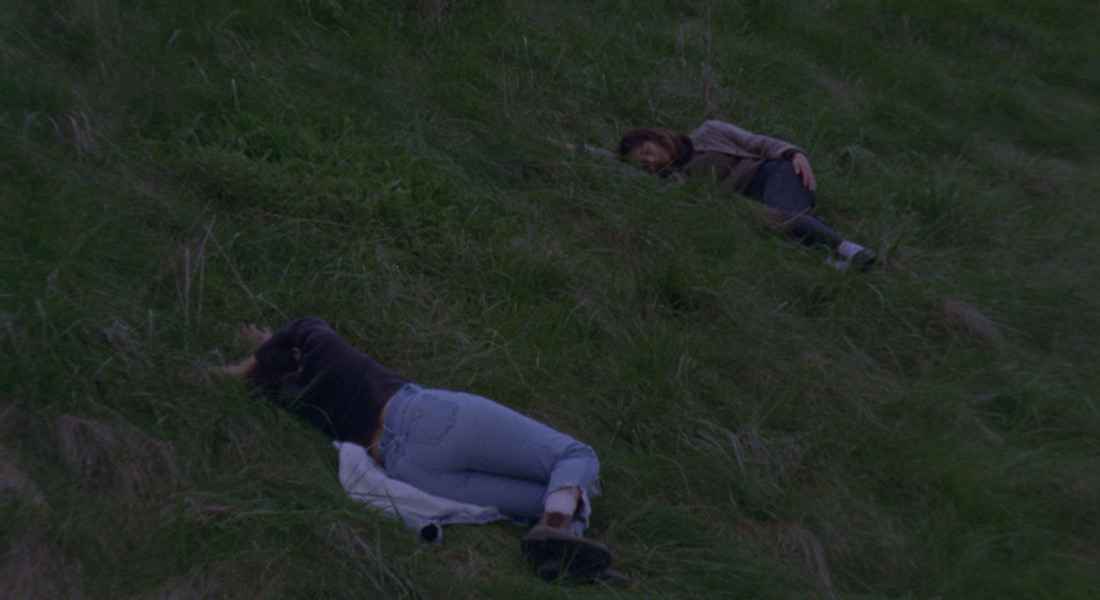 Two women recline on a grassy hillside