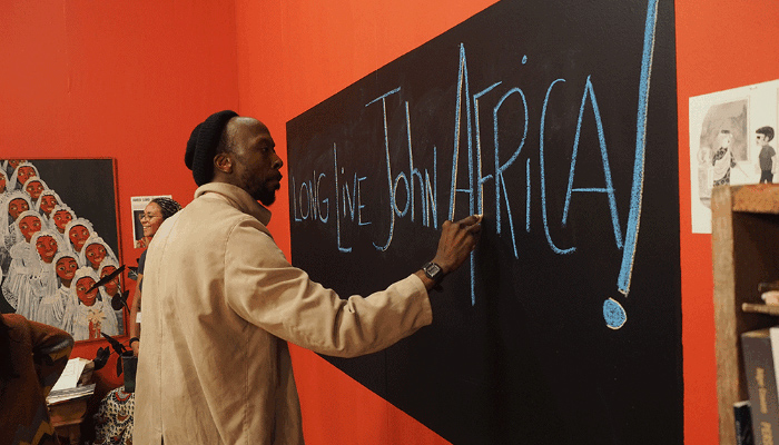 A man writes "Long live John Africa!" on a chalkboard.