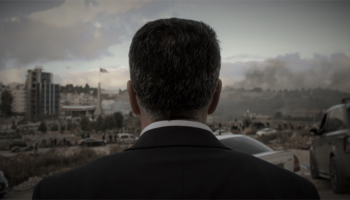 A man in a suit, seen from behind and from the shoulders up, looks out over a hazy city landscape.  