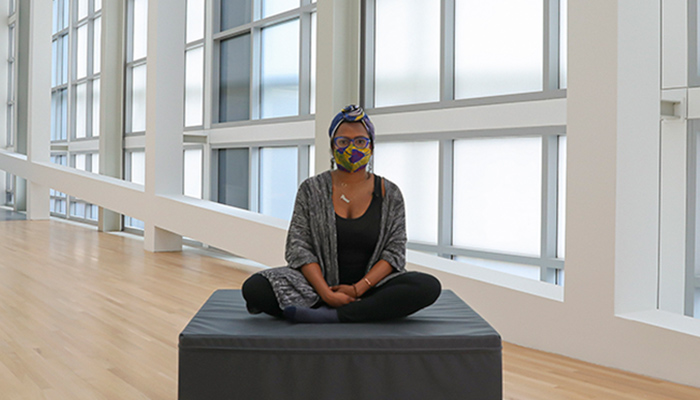 A woman sits on a foam block in the center of an empty gallery space. 